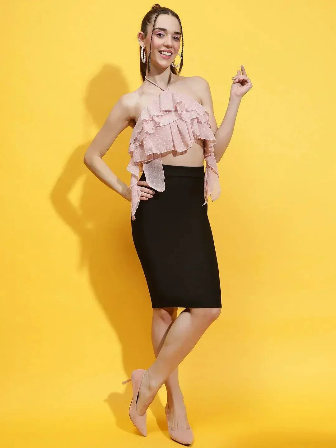 Woman wearing pink halter neck crop top with ruffles paired with a black pencil skirt and heels